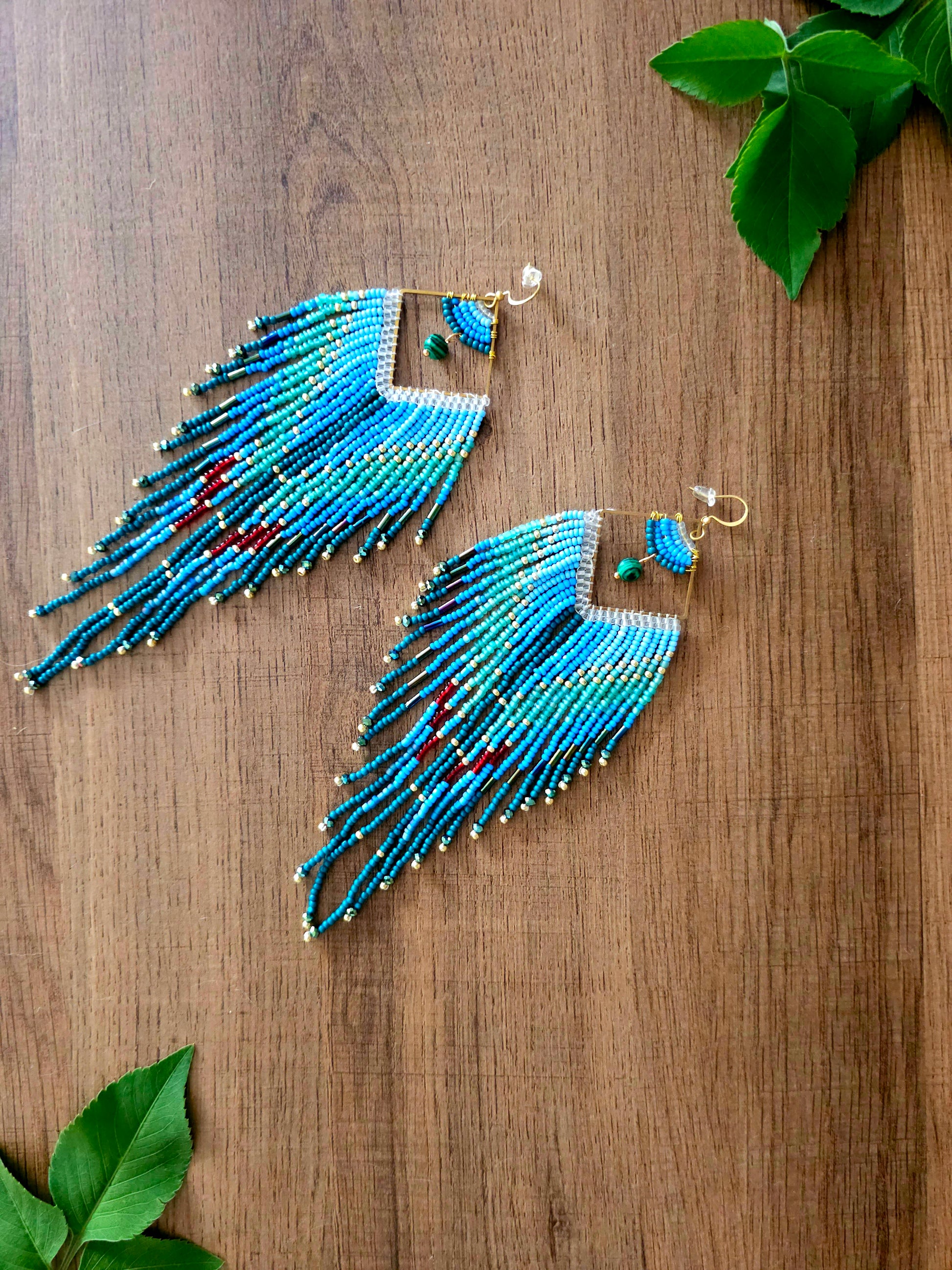The Ocean Cascade Earrings feature a gradient of blue tones, accented by green and red beads. Perfect for adding coastal charm with their flowing fringe design.