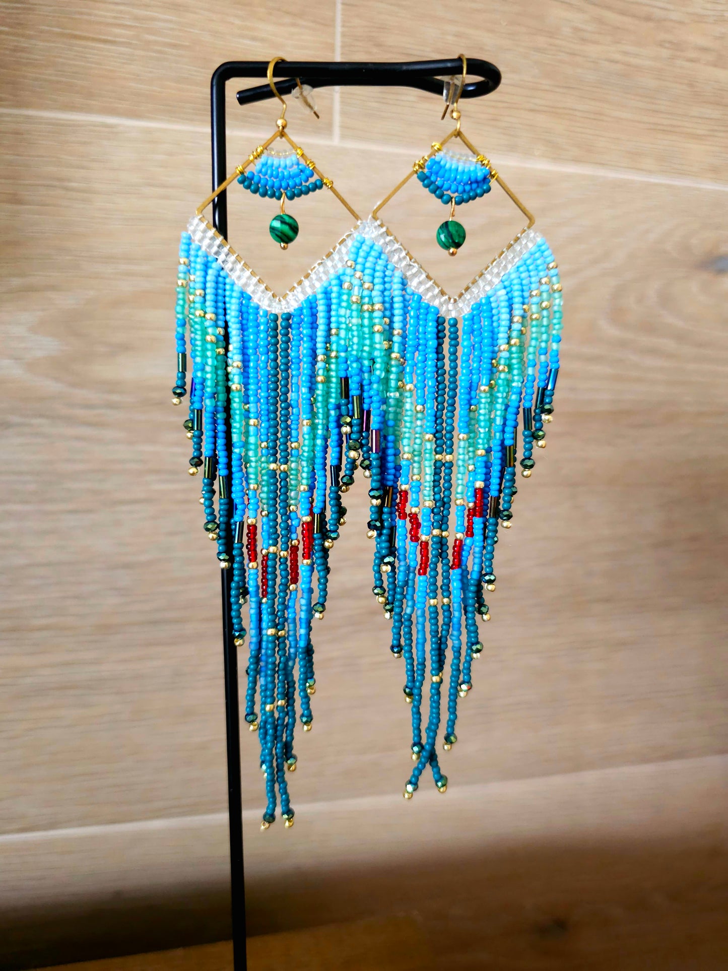 The Ocean Cascade Earrings feature a gradient of blue tones, accented by green and red beads. Perfect for adding coastal charm with their flowing fringe design.